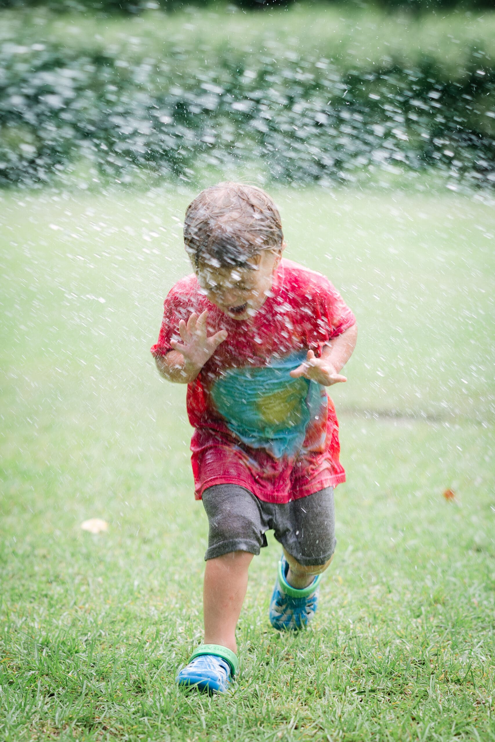 Smiling child running through a sprinkler on a hot summer day, captured by children's photographer in Tallahassee & Bainbridge.