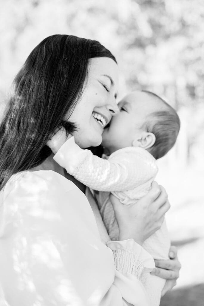 Black and white photo of a joyful mother laughing as her baby kisses her during a natural motherhood photography session in Bainbridge, Georgia