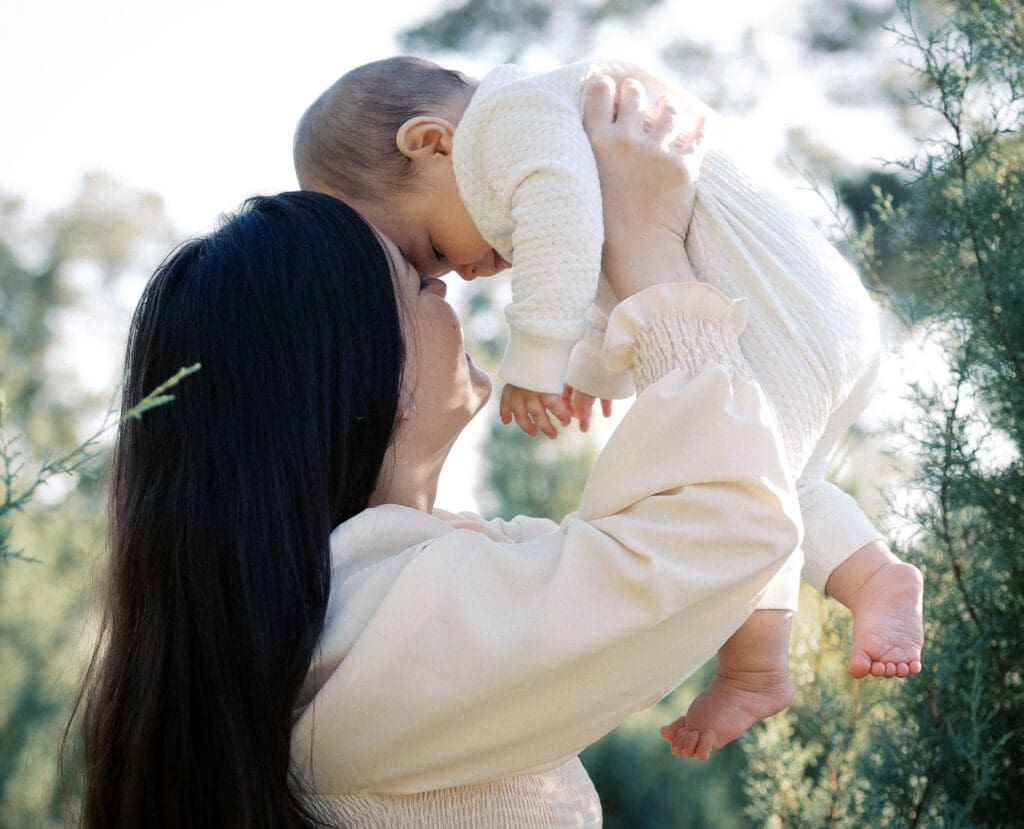 A mother lovingly holds her baby up, their foreheads touching in an intimate, tender moment—one that will be held forever in a portrait.