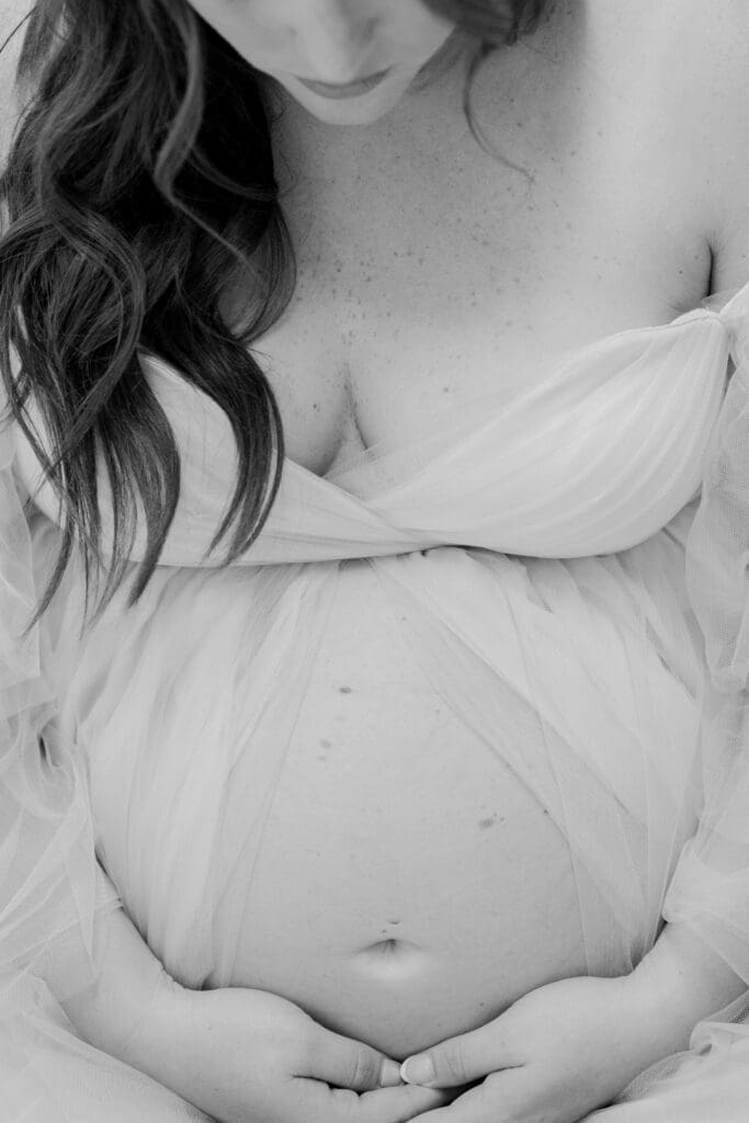Black and white maternity photo showing mother's exposed belly in studio session in Bainbridge