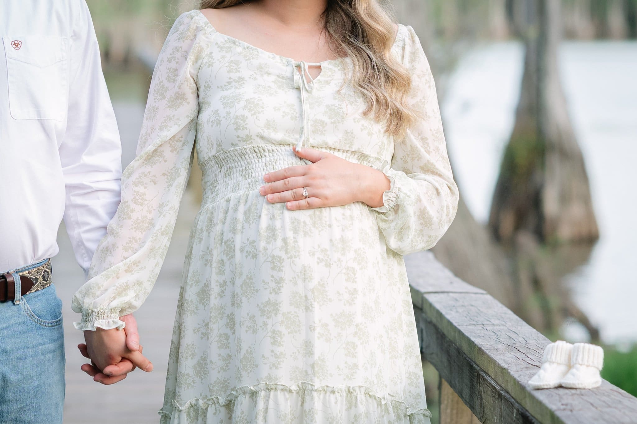 Artistic maternity photo of mother holding her belly and her husband's hand, serving women through motherhood photography