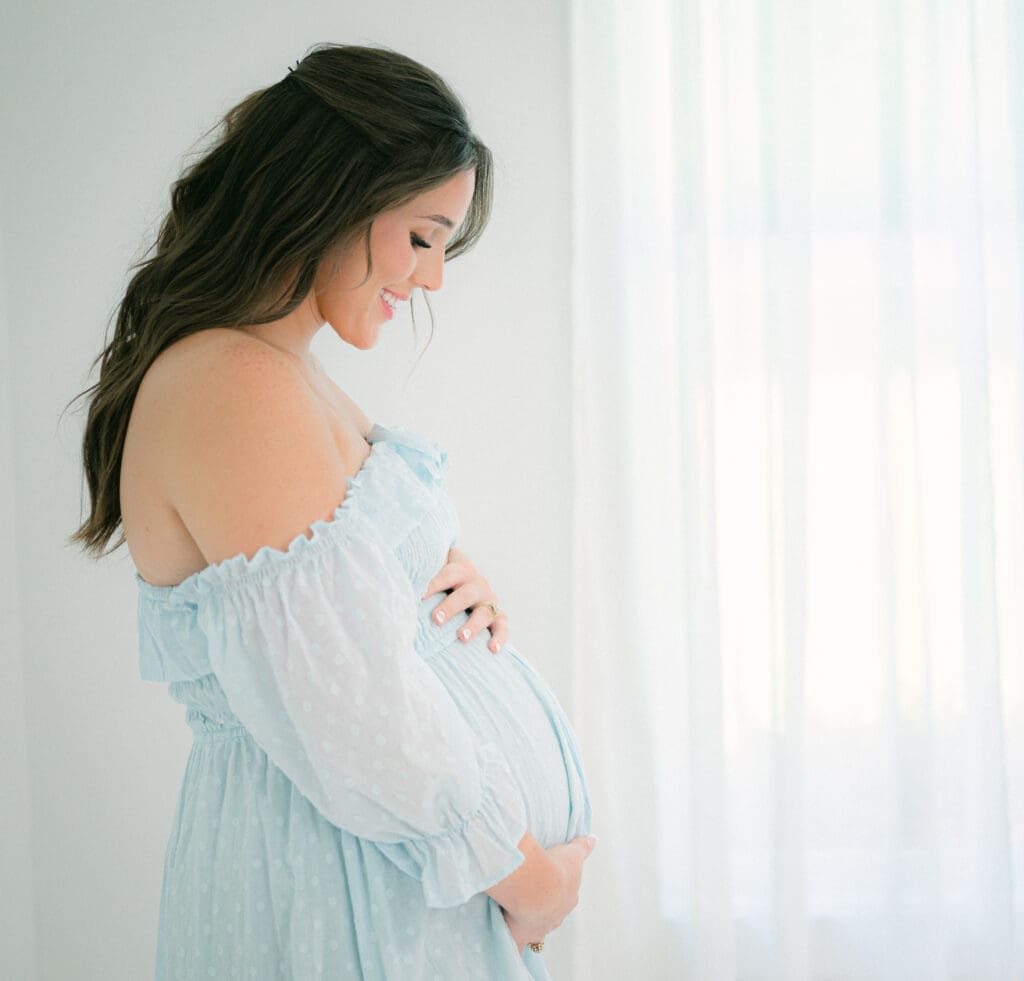 Pregnant mother in a flowing blue dress holding her belly and smiling during a Bainbridge maternity photography session.