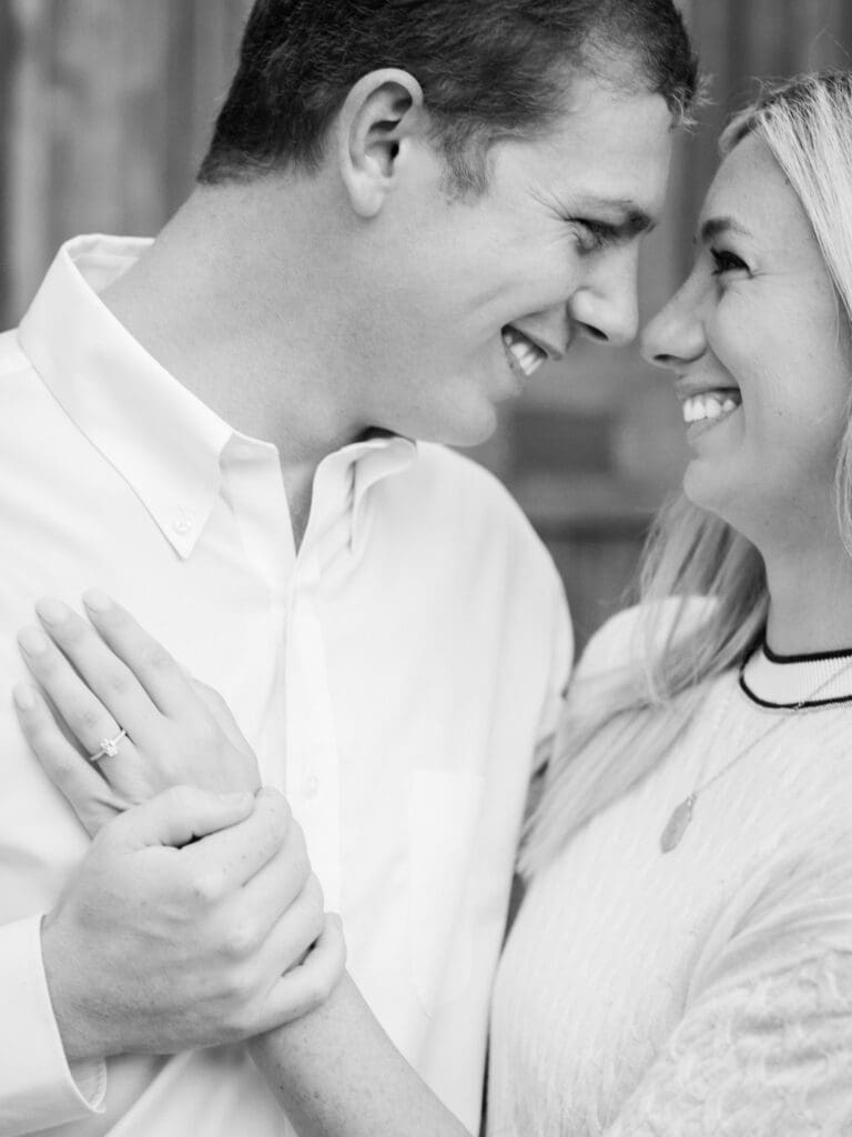 Black and white close-up of couple laughing and holding hands during proposal