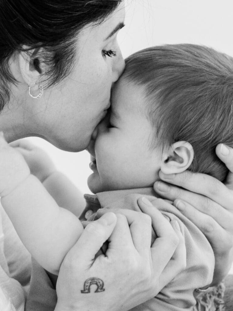 Mother gently kissing her baby in a black and white portrait, capturing a tender motherhood moment