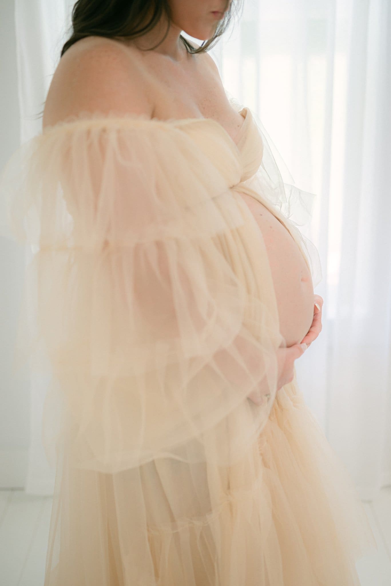 Fine art maternity portrait in studio with soft tulle styling and intimate motherhood lighting