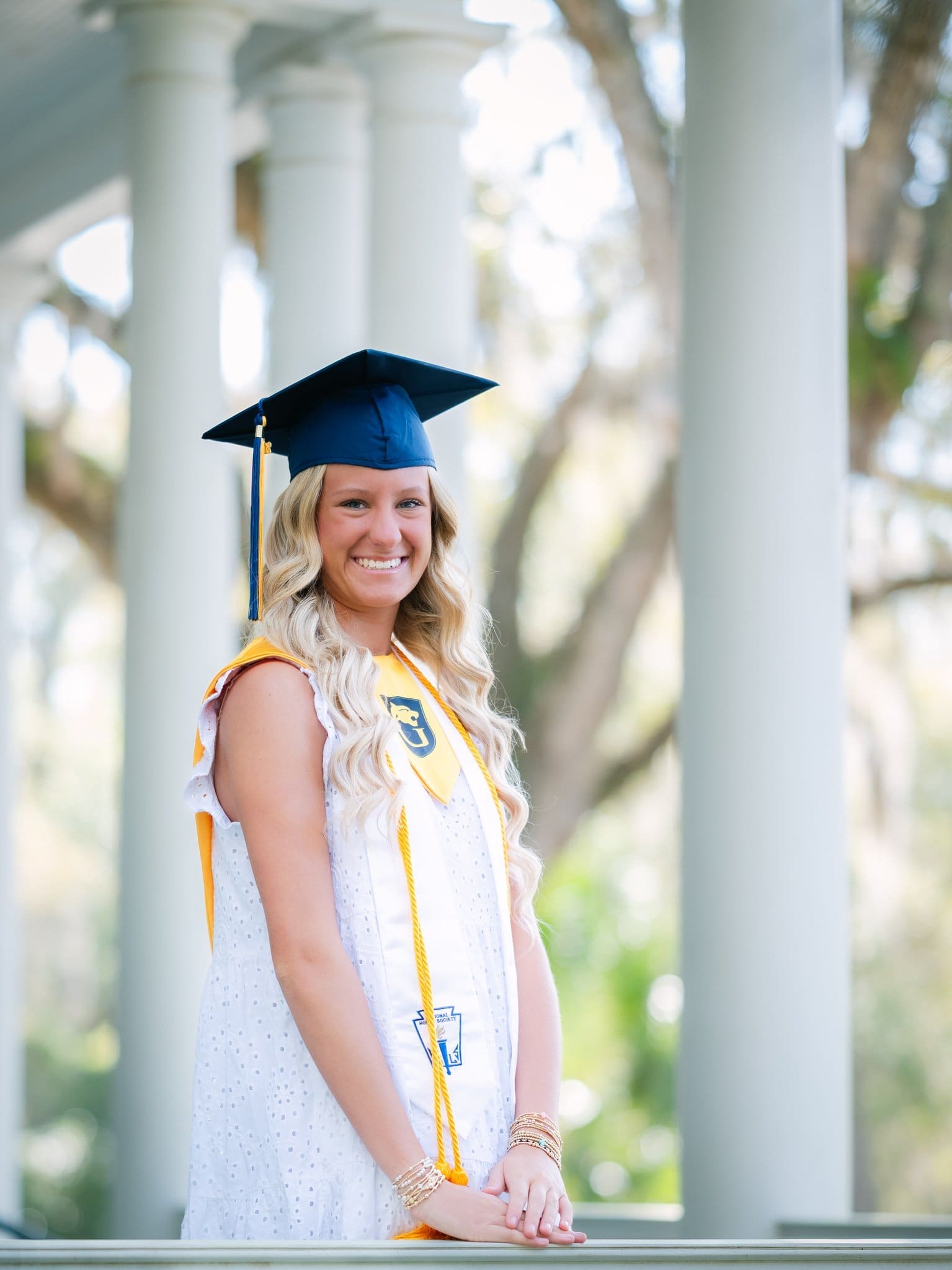 Senior portrait capturing a graduate outdoors celebrating with cap, stole, and honor cords