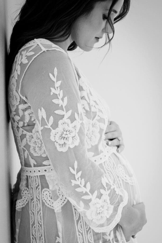 Black and white intimate maternity portrait showing expectant mother looking down at her belly