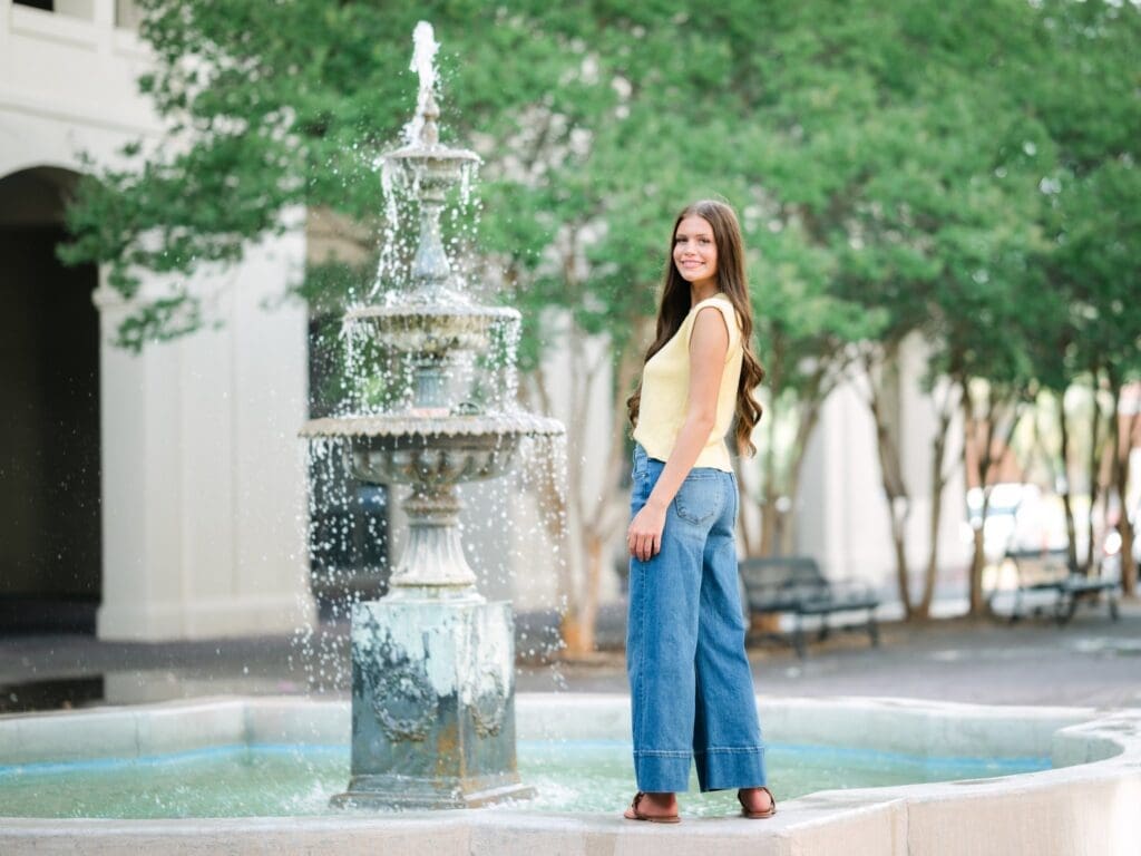 Smiling high school senior standing in front of a fountain during a senior portrait session in Tallahassee, Florida.