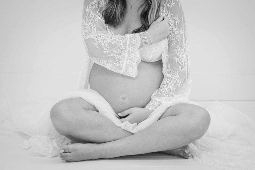 Black and white portrait of pregnant woman sitting and holding her belly during a maternity photography session.