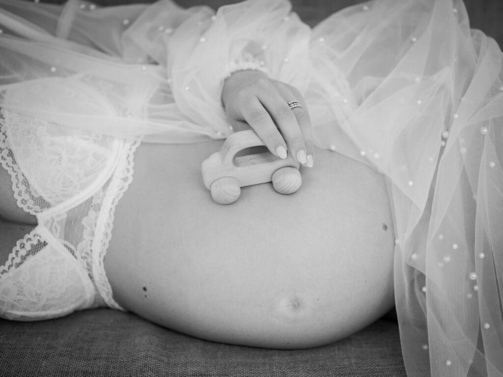 Black and white maternity portrait of expecting mother lying on a sofa with a wooden toy resting near her pregnant belly.