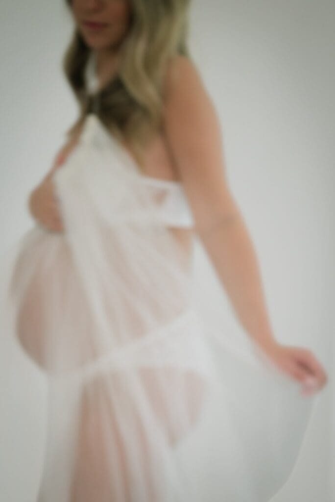 Expecting mother holding a flowing wedding veil during an intimate maternity portrait session.